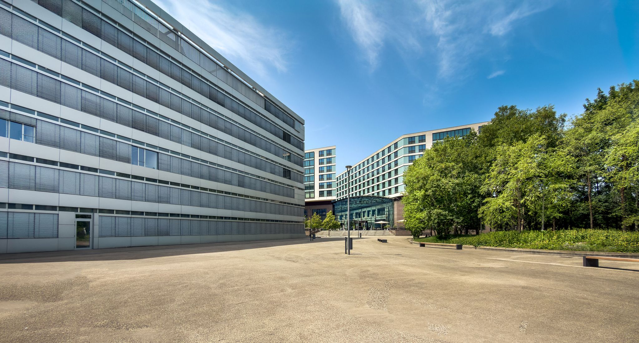 Contemporary office buildings surrounded by lush greenery under a clear blue sky.